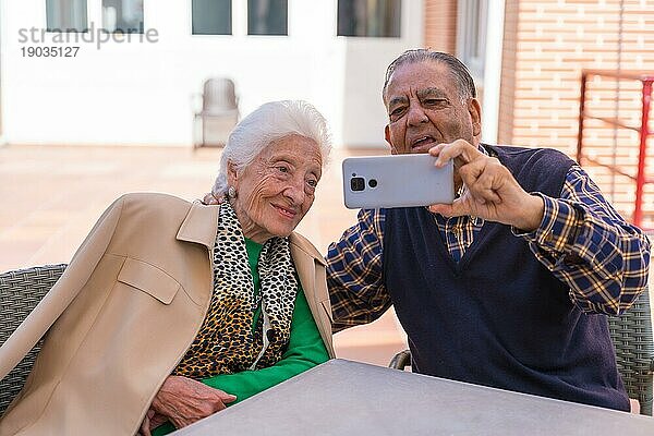 Zwei sehr glückliche ältere Menschen im Garten eines Pflegeheims  die auf das Telefon schauen