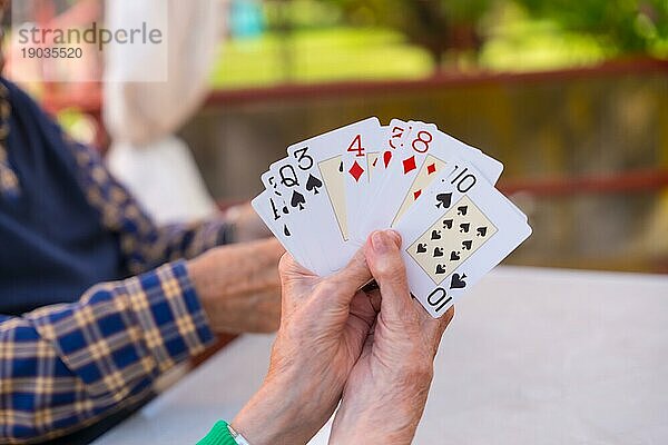 Hände zweier älterer Menschen im Garten eines Pflegeheims oder Seniorenheims  die an einem Sommermorgen Karten spielen