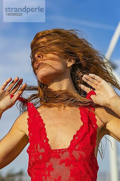 Ein schönes rothaariges Modell posiert oben ohne im Freien mit Windturbinen im Hintergrund