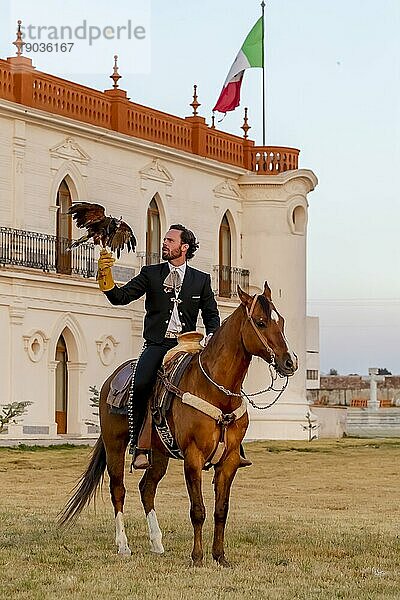 Ein stattlicher mexikanischer Charro posiert vor einer Hazienda in der mexikanischen Landschaft und hält einen Falken