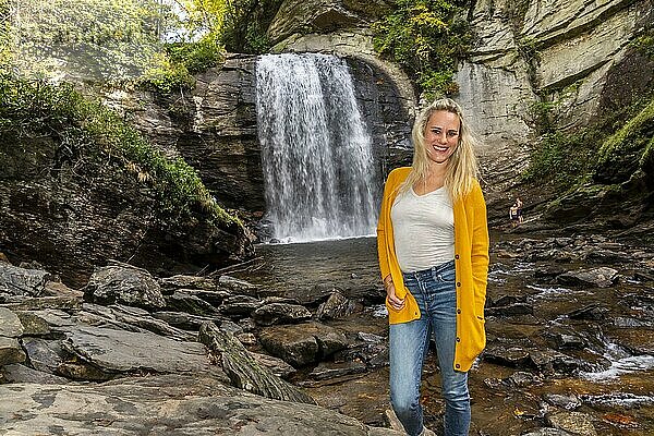 Ein wunderschönes blondes Model genießt einen Herbsttag im Freien mit einem Wasserfall im Hintergrund
