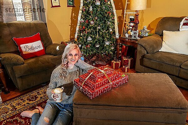 Ein wunderschönes blondes Model genießt die Feiertage zu Hause mit einem Weihnachtsbaum und Geschenken