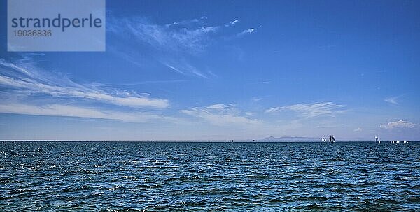Schöne Meereslandschaft an einem hellen Sommertag mit wenigen Segelbooten in der Ferne  großer Himmel mit dynamischen Wolken. Friedlicher Urlaub  meditativer  entspannender Blick. Wochenende am Meer  Strand  Kontemplation