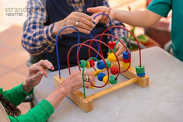 Die Hände zweier älterer Menschen im Garten eines Pflegeheims oder Seniorenheims  die mit Spielen zur Verbesserung der Beweglichkeit der Hände spielen