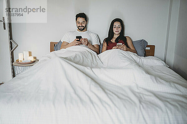 Junges Paar im Bett und schaut auf sein Smartphone