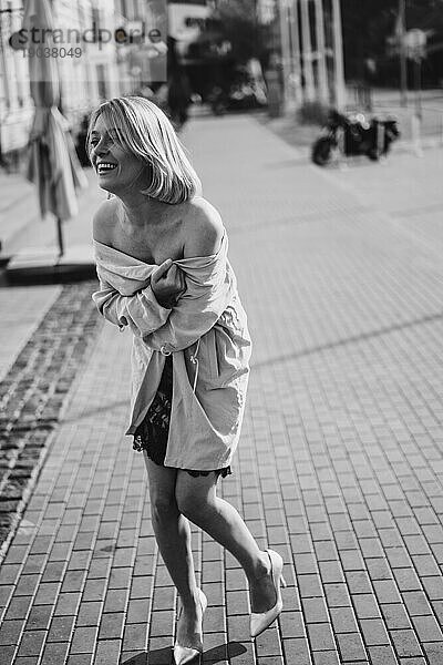 Schöne blonde Frau in einem Spitzenkleid auf einer Stadtstraße  glückliches Lächeln.