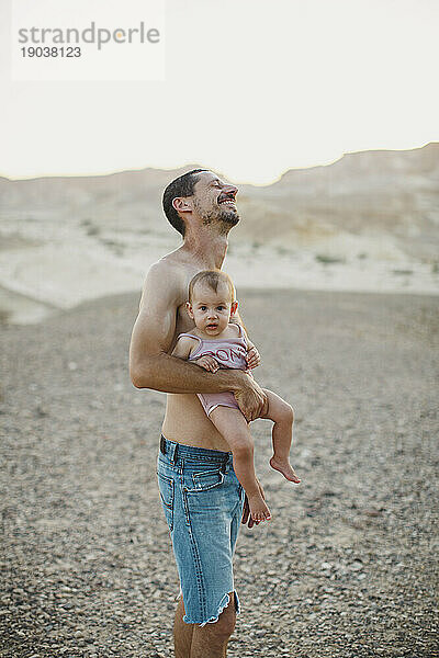 Ein Vater lacht  während er sein kleines Mädchen in der Wüste hält