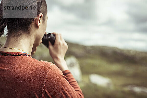 Wanderin schaut durch ein Fernglas in den schottischen Bergen