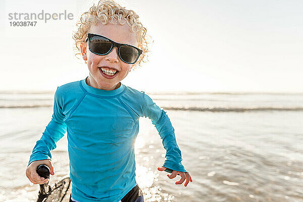 Porträt eines lockigen  glücklichen Jungen mit Grübchen und Sonnenbrille