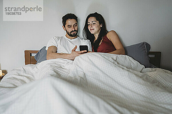 Junges Paar im Bett und schaut auf das Smartphone