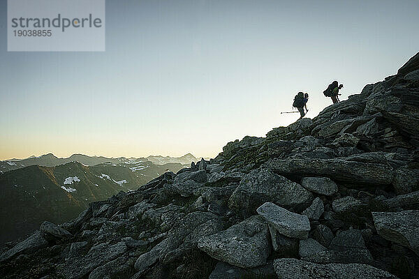 Silhouette zweier männlicher Wanderer bei Sonnenuntergang mit Bergen im Hintergrund