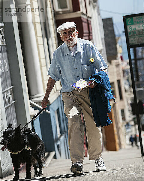 Ein älterer Mann geht mit seinem Hund eine Stadtstraße entlang.
