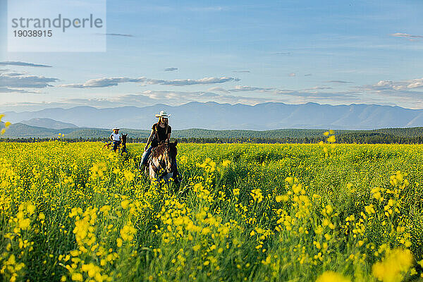 Zwei Cowgirls reiten bei Sonnenuntergang durch ein Rapsfeld