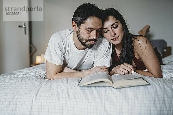 Liebespaar liest zu Hause im Bett ein Buch und entspannt sich