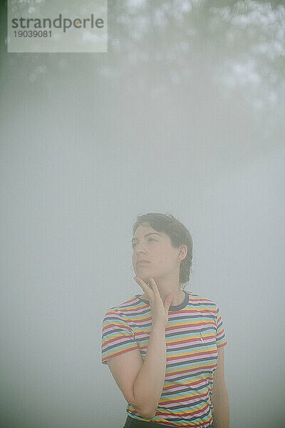 Young woman in a foggy park looking up toward the sky