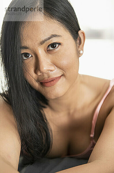 Schöne thailändische Frau posiert im rosafarbenen Nachthemd auf dem Bett