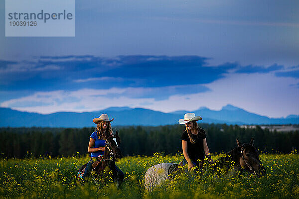 Zwei Cowgirls reiten bei Sonnenuntergang durch ein Rapsfeld