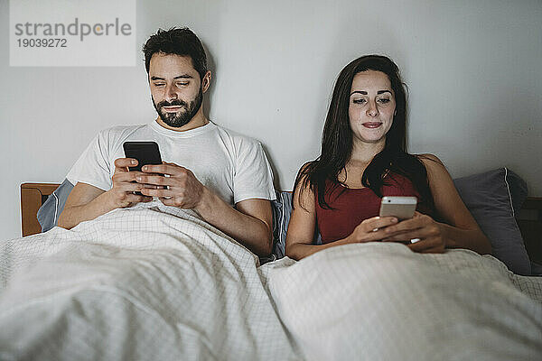 Junges Paar im Bett und schaut auf sein Smartphone