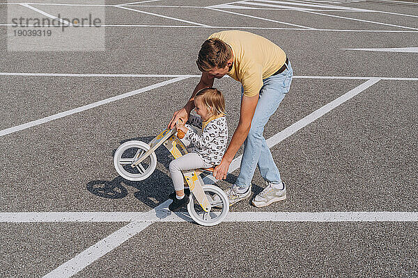 Ein junger Mann fährt ein kleines Mädchen auf einem hölzernen Laufrad