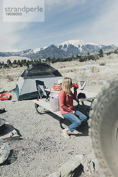 Einsame Camperin trinkt aus einer Solo-Tasse an einem Picknicktisch auf dem Campingplatz