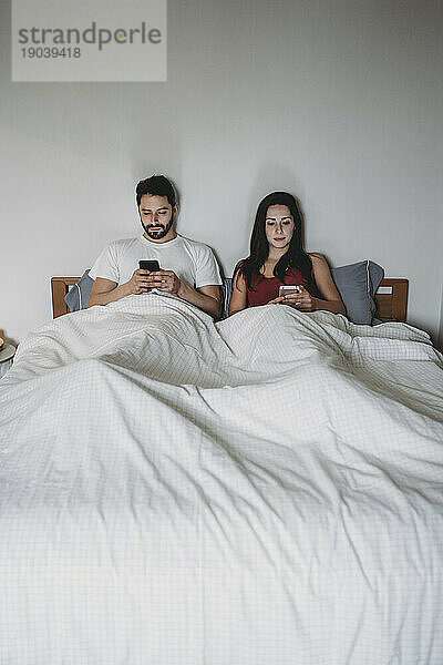 Junges Paar im Bett und schaut auf sein Smartphone