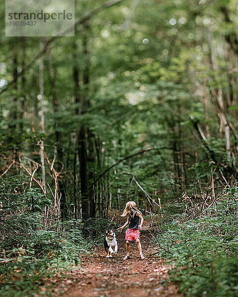 Junges Mädchen rast mit ihrem australischen Schäferhund durch einen Wald