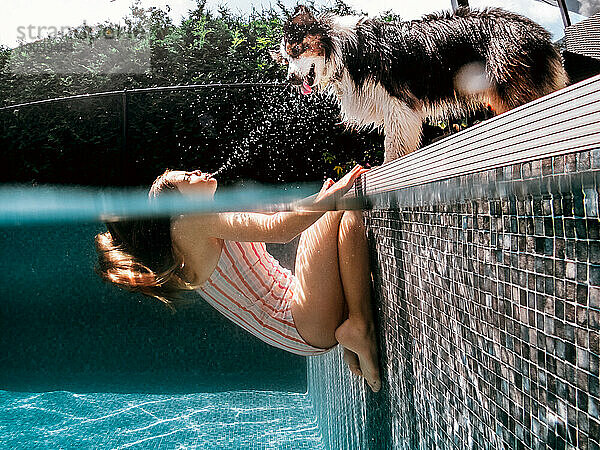 Lustiges Bild eines Mädchens im Pool  das seinen Hund mit Wasser bespritzt