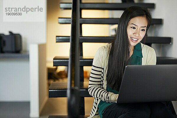 Lächelnde  selbstbewusste Geschäftsfrau  die einen Laptop benutzt  während sie auf der Treppe im Büro sitzt