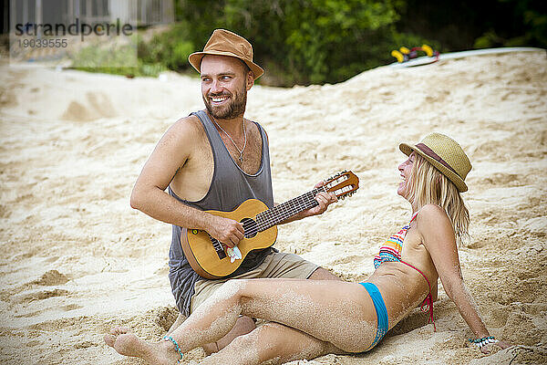 Junges Paar mit Ukulele am Strand.