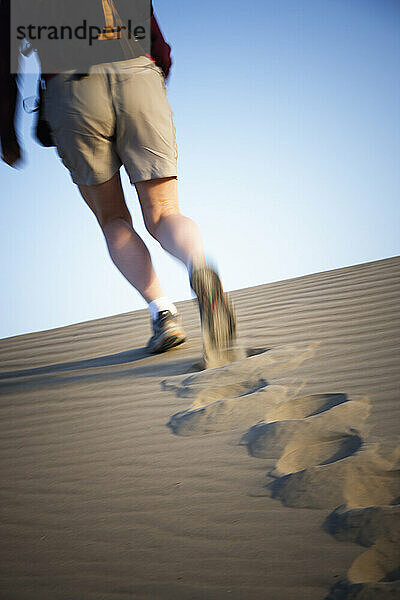 Rückansicht der Beine einer Frau  die eine Sanddüne im Death Valley National Park  Kalifornien  hinaufgeht.