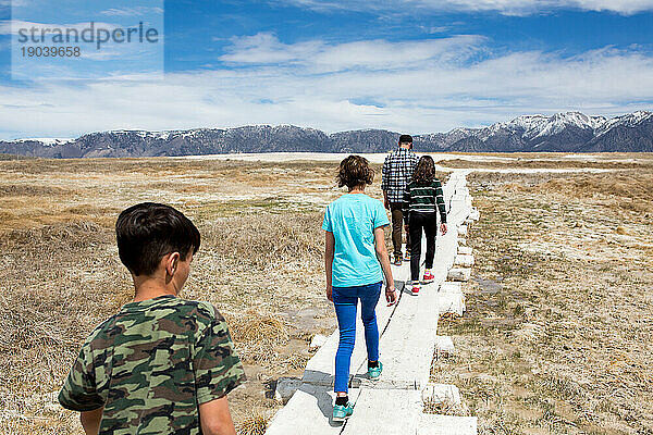 Vater und drei Kinder gehen auf einem mit Brettern versehenen Weg in Richtung Berge