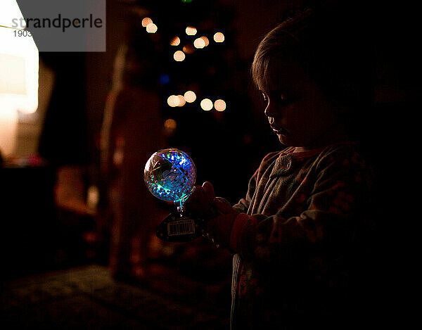 Baby/Kleinkind hält leuchtendes Spielzeug mit Weihnachtsbokeh