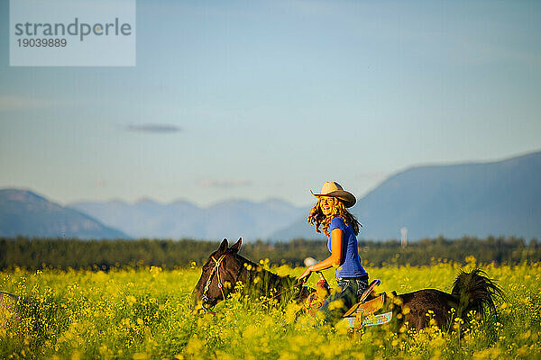 Mädchen lacht zu Pferd durch ein Rapsfeld in Montana