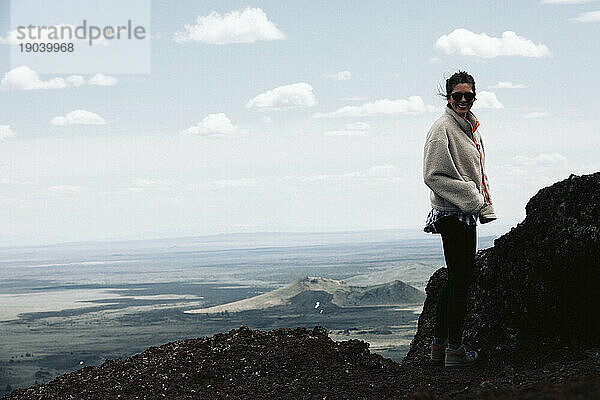Wandernde Frau in Fleece lächelt in die Kamera auf einem markanten Vulkan