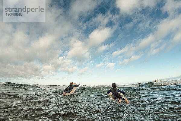 Zwei heranwachsende Geschwister paddeln auf Surfbrettern über Wellen