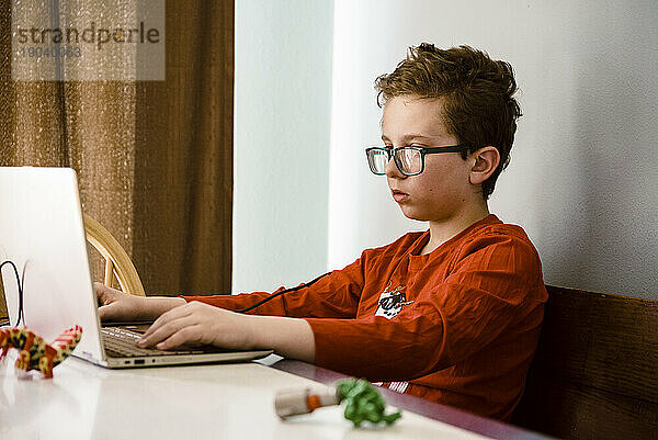 Junge in einem roten Hemd  der drinnen einen Computer benutzt.