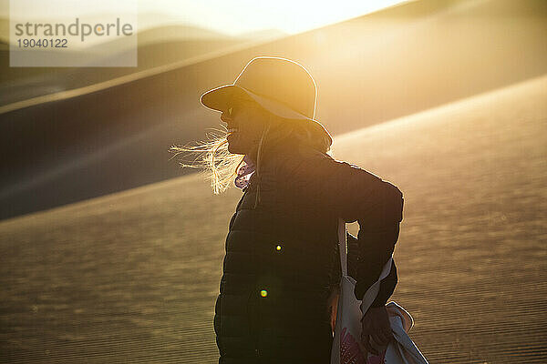Profilporträt einer Abenteurerin mit Filzhut bei Sonnenuntergang in den Dünen