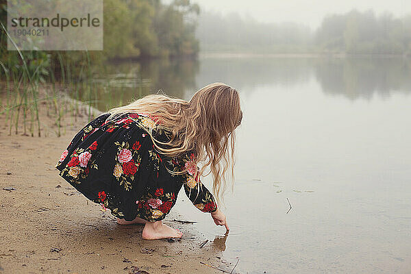 Kleines Mädchen taucht auf einem einsamen und nebligen Abenteuer mit dem Finger in den Teich