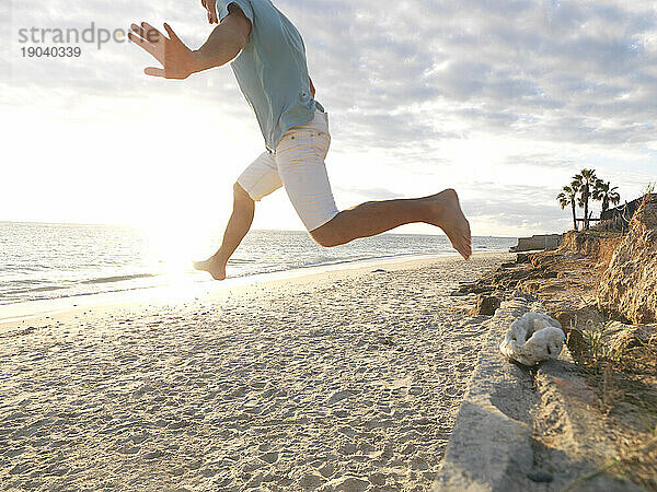 Reifer Mann springt bei Sonnenaufgang an den Strand