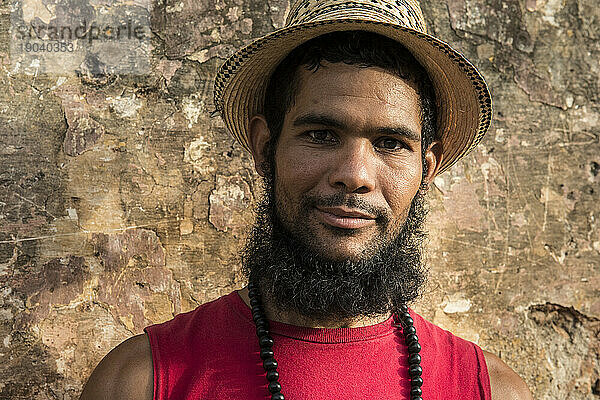Ein lächelnder junger kubanischer Mann mit Bart steht vor einer alten Steinmauer in Trinidad  Kuba