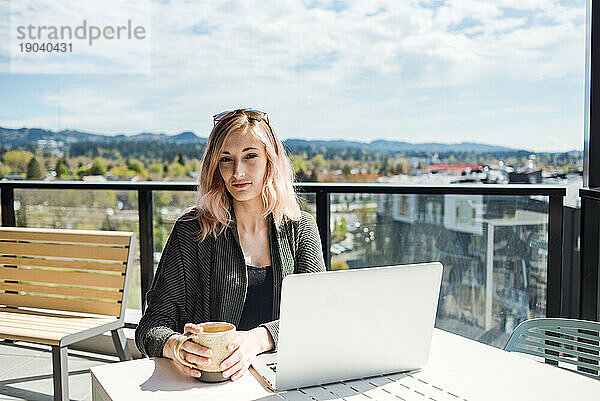 Porträt einer Frau  die draußen mit Laptop in die Kamera blickt