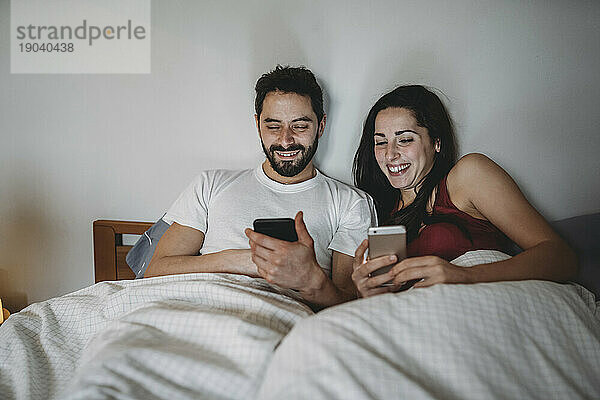 Junges Paar im Bett und schaut auf sein Smartphone