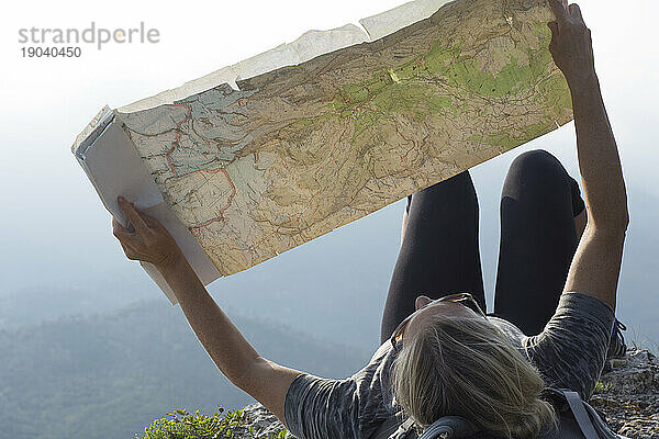 Reife Wanderin liegt mit Karte am Rand einer Klippe