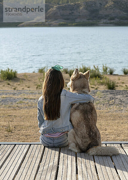 Mädchen entspannt sich mit ihrem Haustier Husky an einem See und beobachtet den Sonnenuntergang