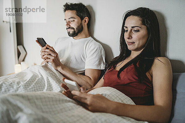 Junges Paar im Bett und schaut auf sein Smartphone