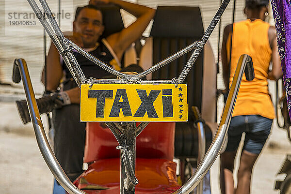 Der Lenker eines kubanischen Bicitaxi  an dem ein handgemaltes „TAXI“-Schild hängt. Alt-Havanna oder Habana Vieja  La Habana  Kuba