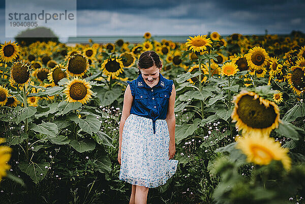 Lächelndes Mädchen beim Spaziergang durch ein Sonnenblumenfeld