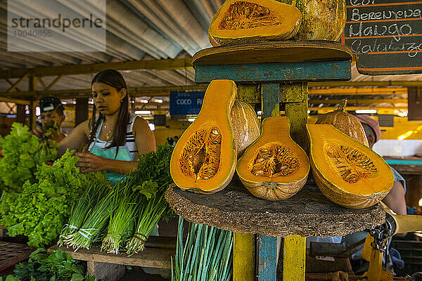Calabaza auf einem Regal mit einer Frau  die Salat im Hintergrund auf einem Lebensmittelmarkt einwickelt - Havanna  Kuba
