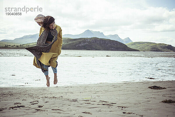 Mädchen im schönen Mantel springt am Strand