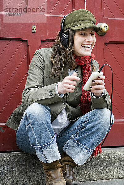 Hippe Frau entspannt sich vor roter Tür  während sie Musik auf dem Ipod hört. Boston  MA.